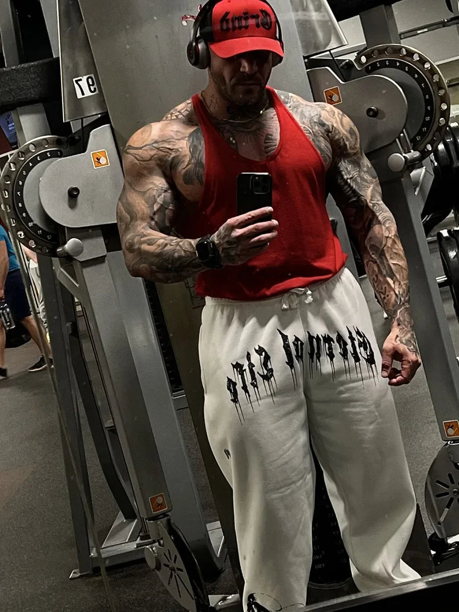 2024 Men’s Sports Pants Casual Gym Training Joggers for New Year worn by a muscular man in a gym mirror selfie.